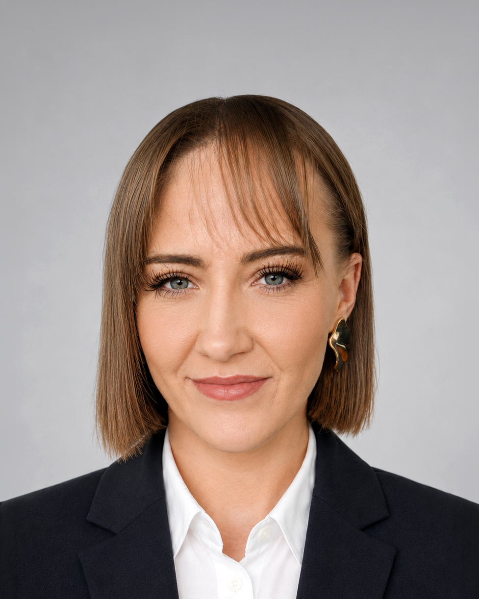 Professional headshot of a woman with short brown hair, wearing a black blazer and white shirt, smiling softly.