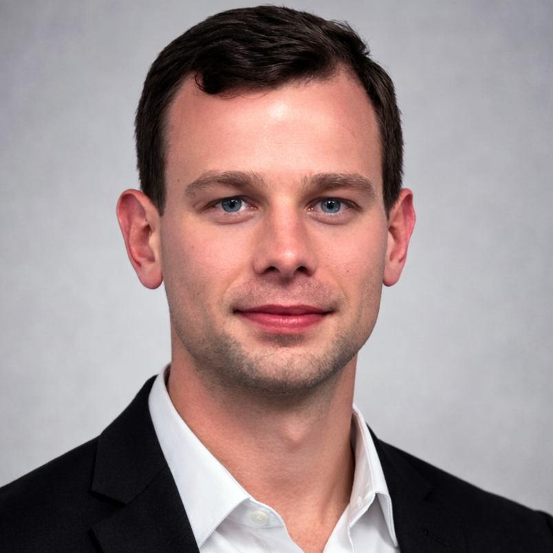 Professional headshot of a man in a black suit and white shirt against a gray background.
