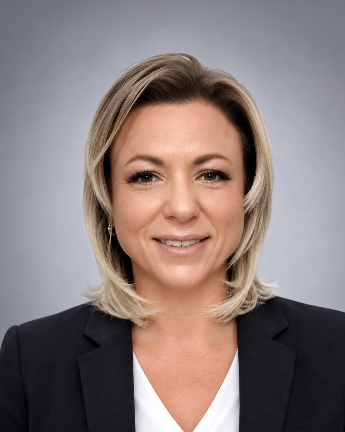 Professional headshot of a smiling woman with blonde hair in a black blazer against a gray background in a corporate setting.